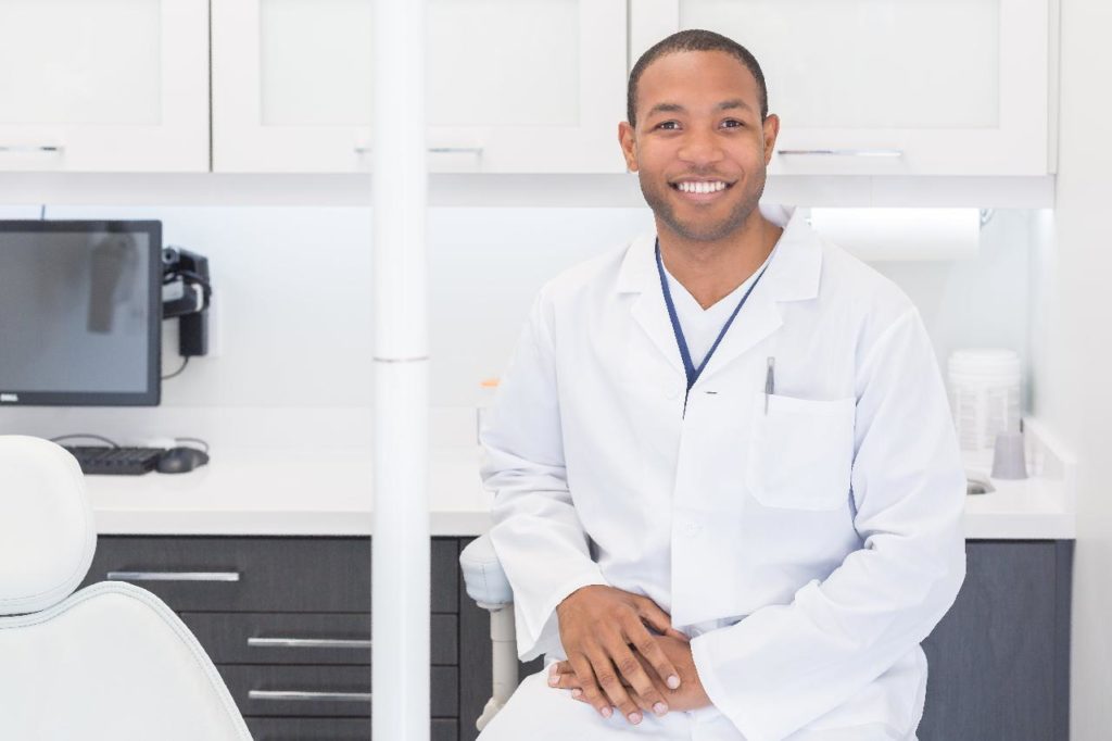 Un hombre sentado en el consultorio de un dentista, observando la capacitación del equipo dental.