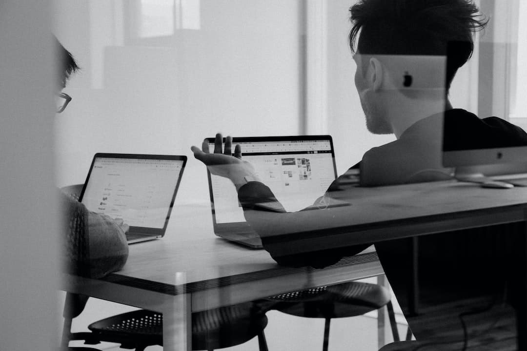 Dos personas sentadas en un escritorio con computadoras portátiles.