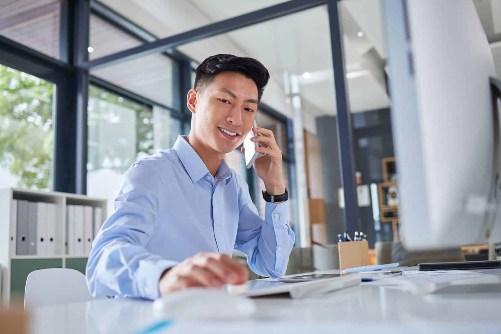 Empresario asiático hablando por teléfono mientras está sentado en su escritorio.