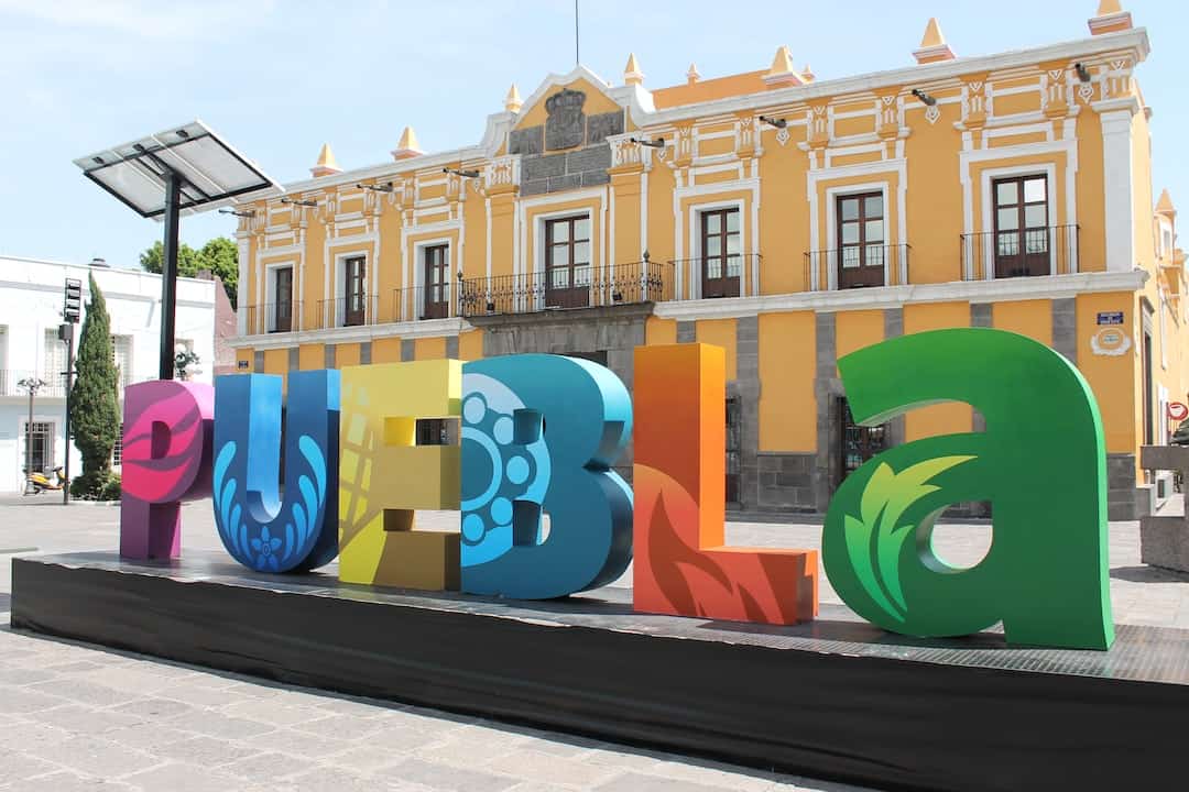 Un letrero colorido con la palabra puebla frente a un edificio. Ideas de Negocios Rentables en Puebla