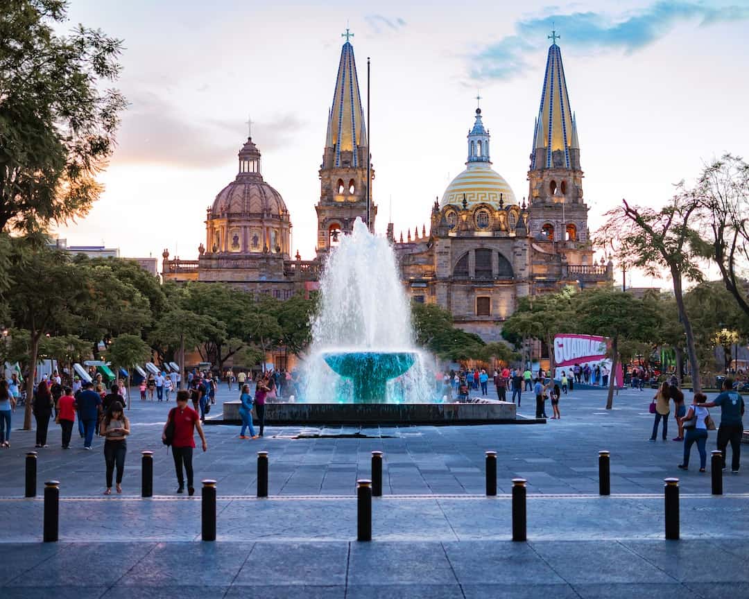 La gente camina alrededor de una fuente frente a una catedral. Ideas de Negocios Rentables en Jalisco