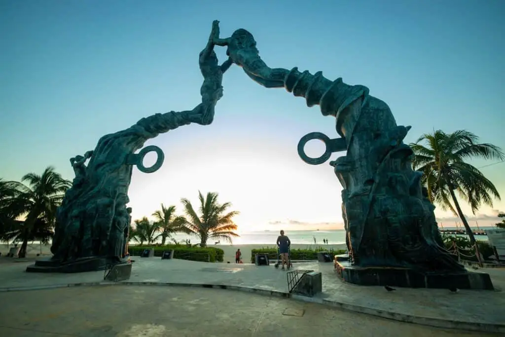 Una estatua de un hombre y una mujer frente a una playa. Ideas de Negocios Rentables en Playa del Carmen