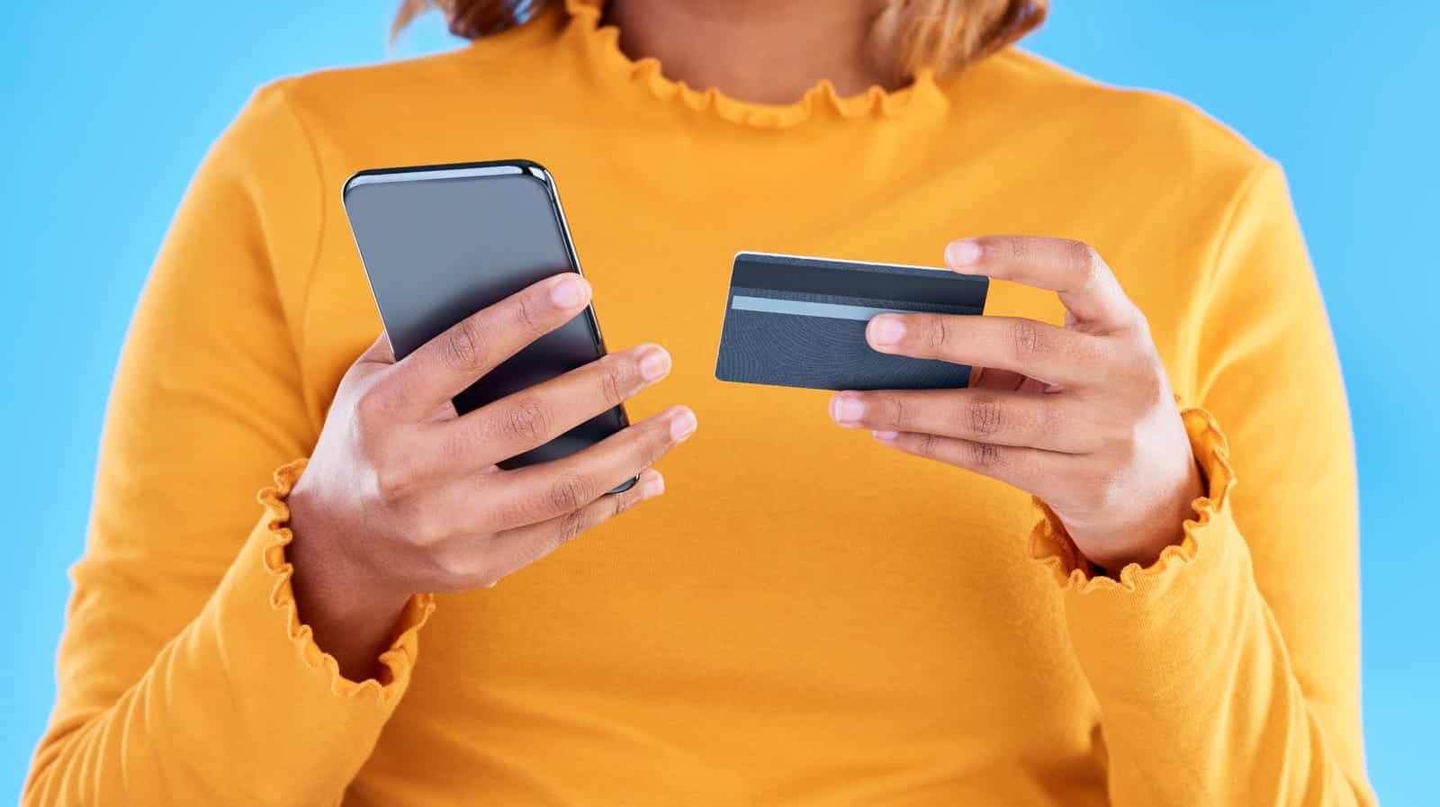 Una mujer sosteniendo una tarjeta de crédito y un teléfono inteligente.