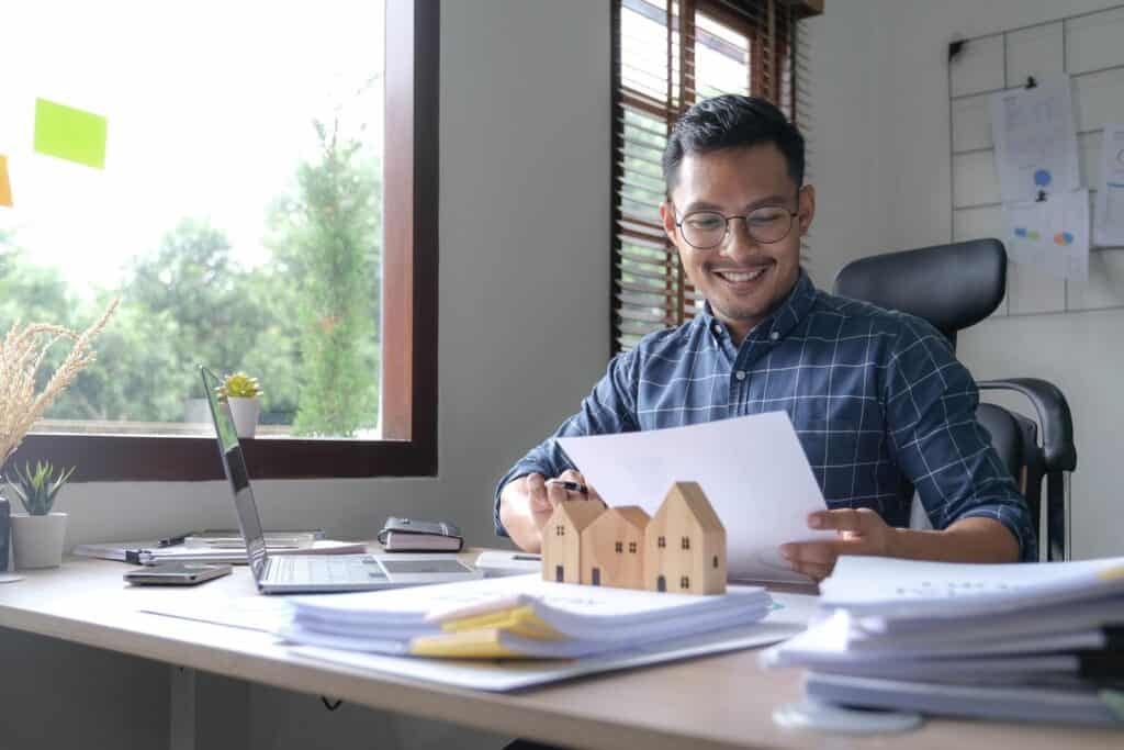 Un hombre de negocios asiático sentado en su escritorio con un modelo de casa frente a él.
