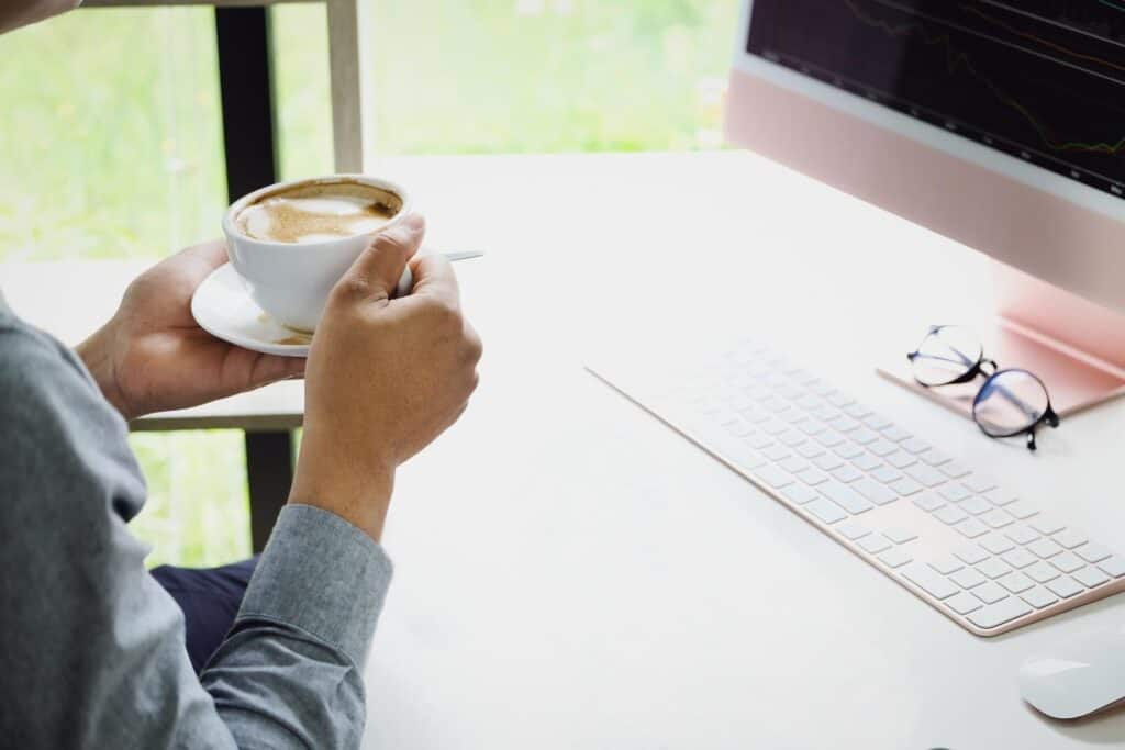 Un hombre tomando una taza de café frente a la pantalla de una computadora.