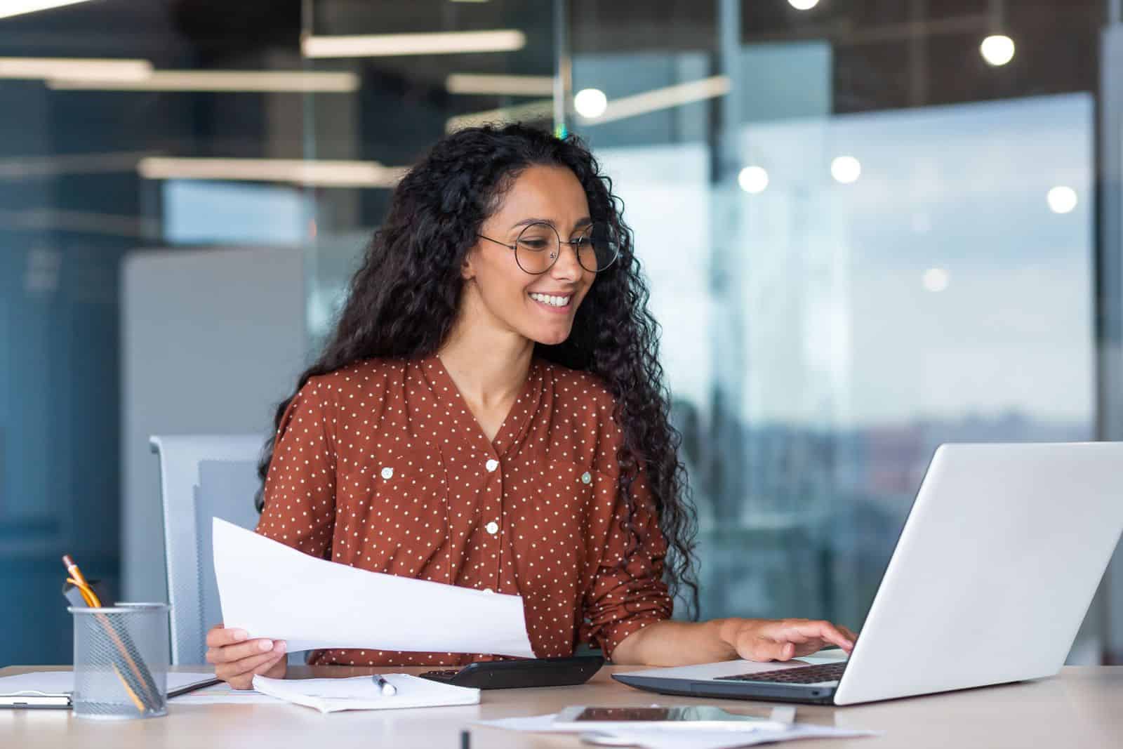 Una mujer sonriente trabajando en una computadora portátil en una oficina.