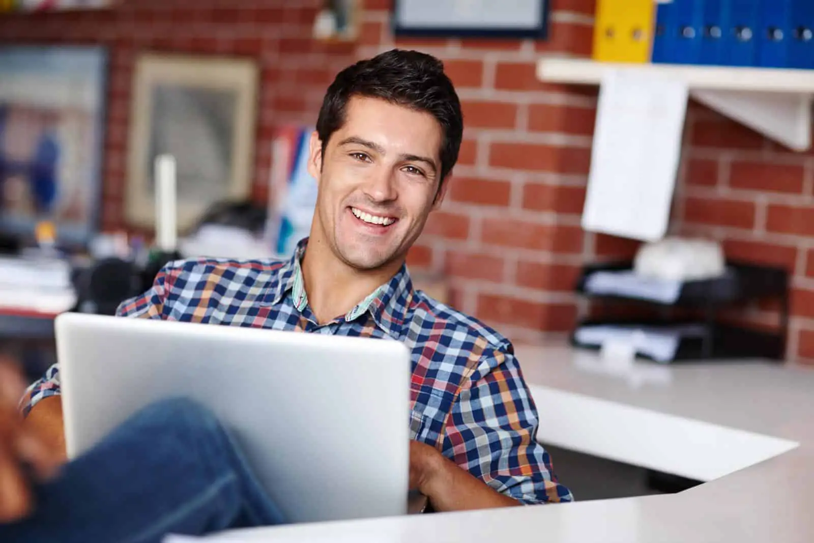 Un hombre sonriente usando una computadora portátil en una oficina.